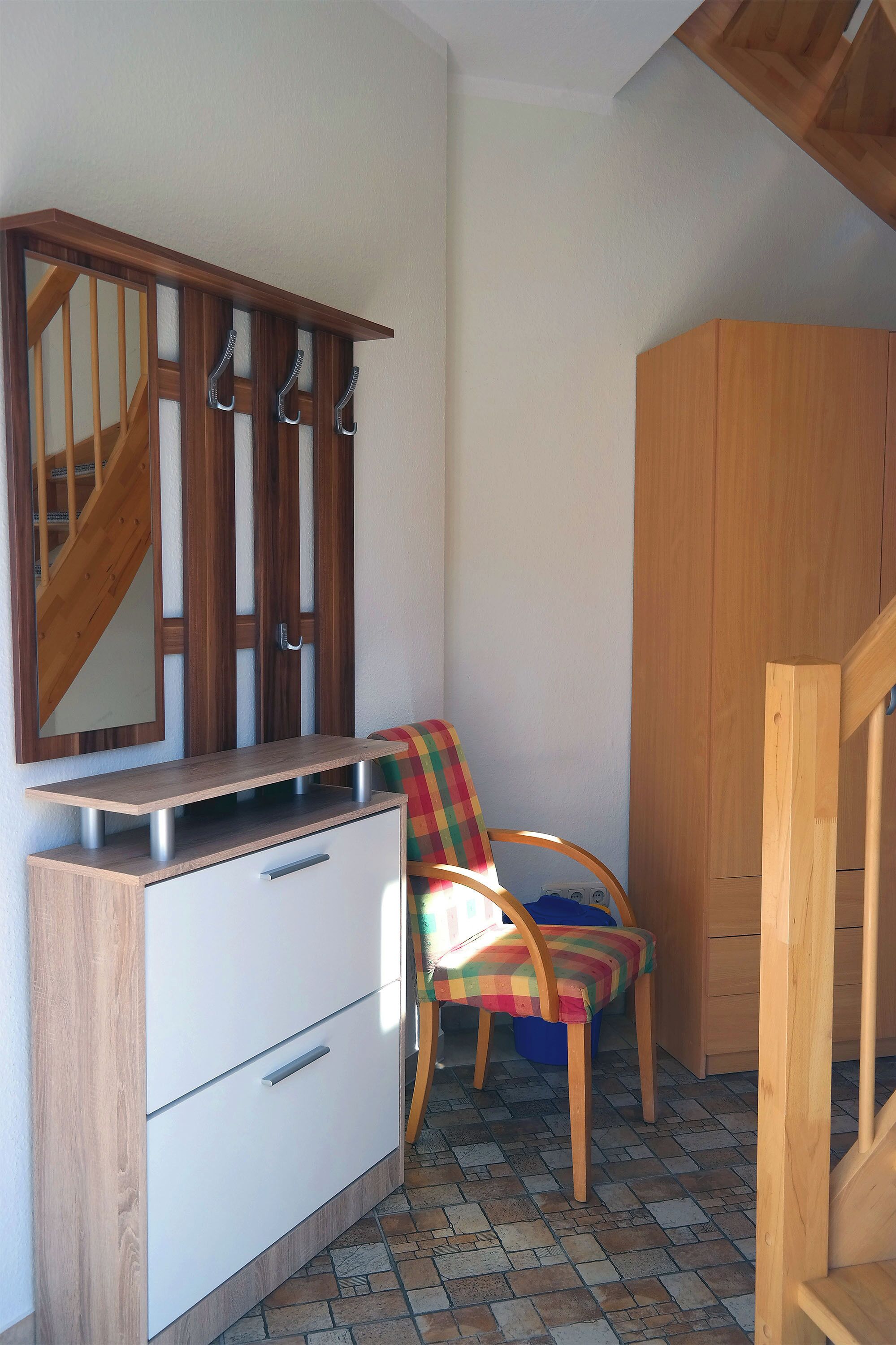 A room with a wooden cabinet, a mirror, a chair with a colorful cushion, and a tiled floor.
