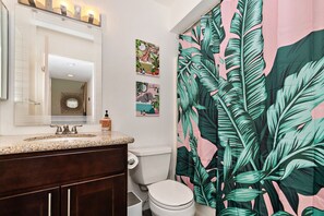 A bathroom with a sink, mirror, toilet, and a shower curtain with a tropical leaf pattern. - Perfect Pool Safari - Palm Springs (Palm Springs)