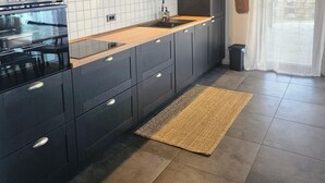 A modern kitchen with dark cabinetry, a white tiled backsplash, and a wooden countertop.