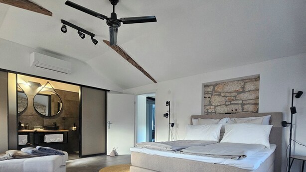 A modern bedroom with a large bed, a built-in wardrobe, a vanity with a mirror, and a ceiling fan.