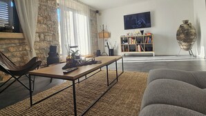 A modern living room with a stone wall, a flat-screen TV, a bookshelf, and a large vase.