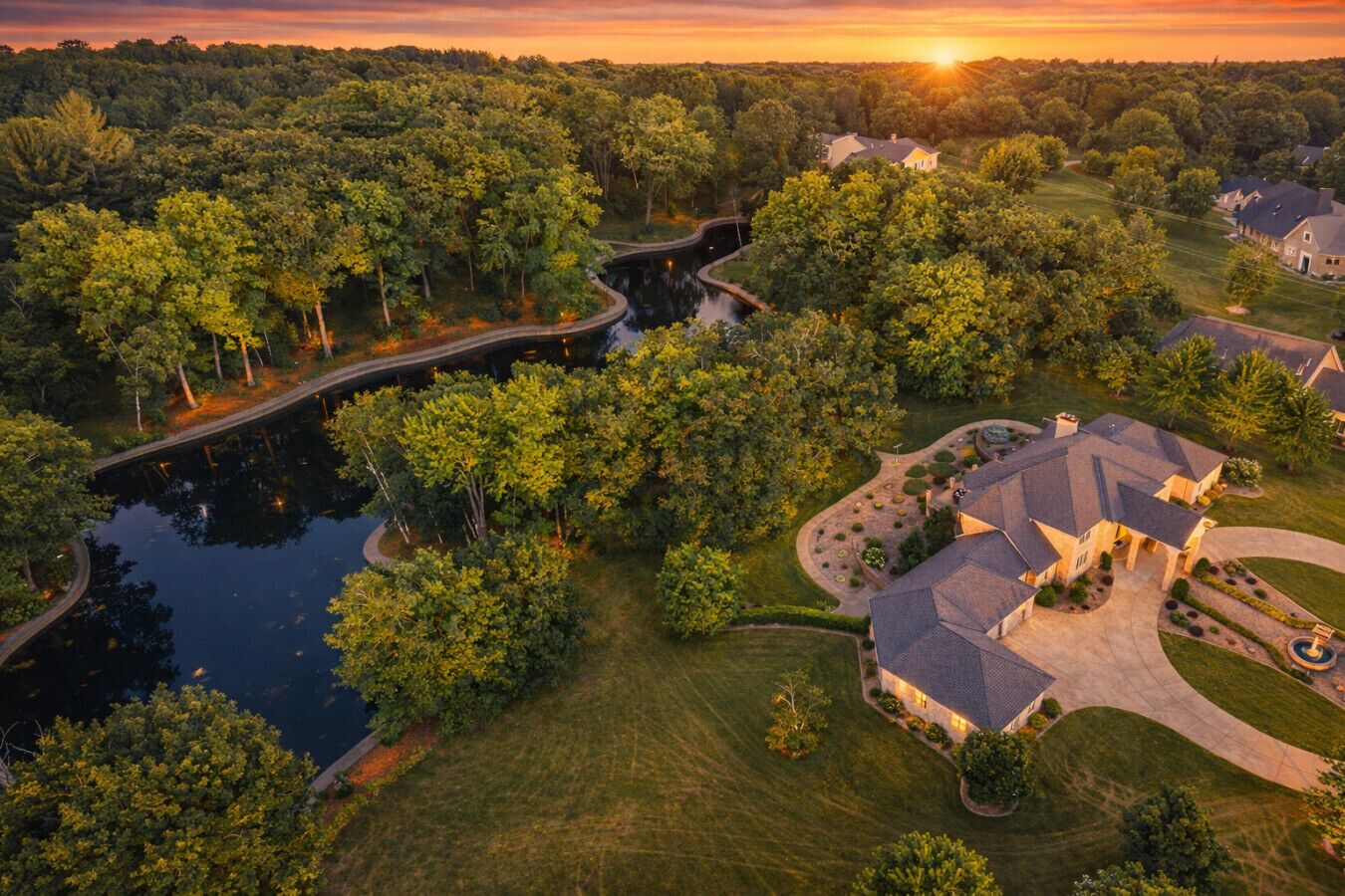 Vue aérienne d’un quartier résidentiel avec une grande maison, un étang et un pont.