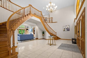 A spacious living area with a wooden staircase, a chandelier, and a view into another room.