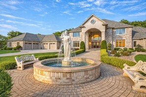 A stone house with a fountain, a driveway, and a well-maintained lawn.