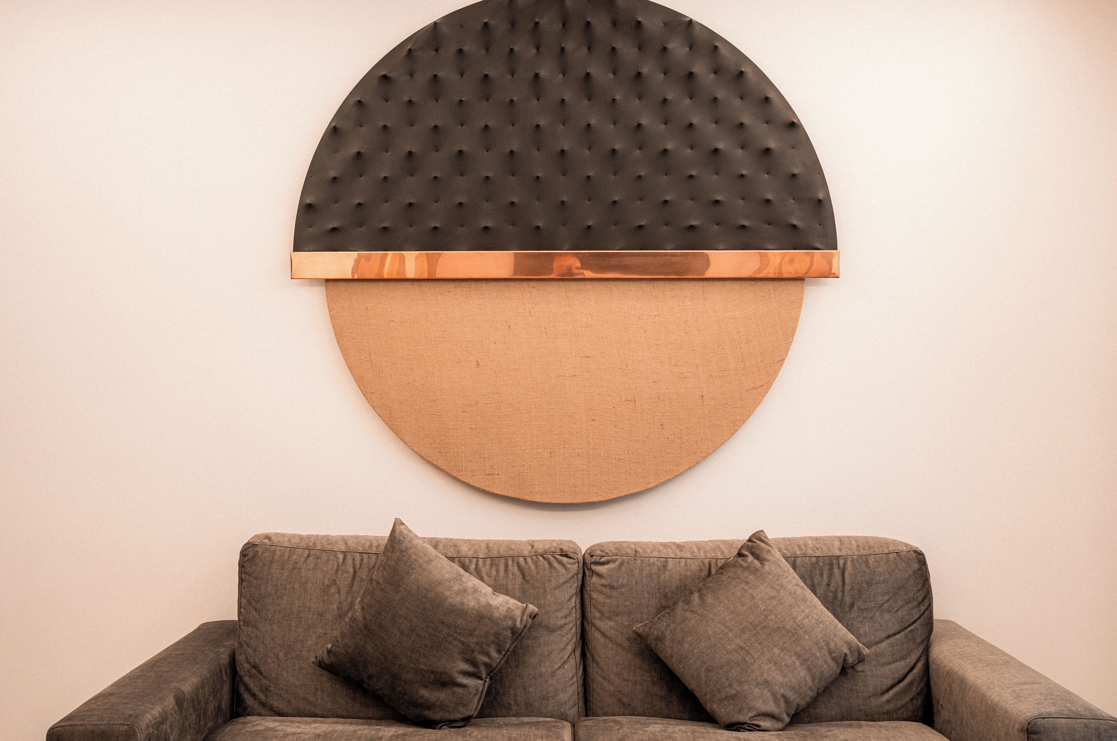 A modern living room with a large, circular wall art piece above a gray sofa with two cushions.