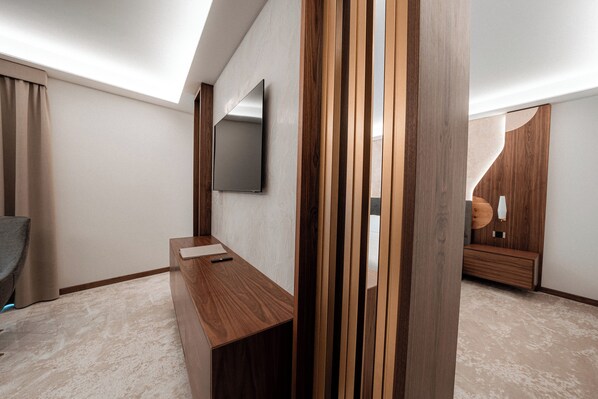 Una habitación de hotel moderna con un escritorio de madera, un televisor de pantalla plana montado en la pared y un ventanal con cortinas.