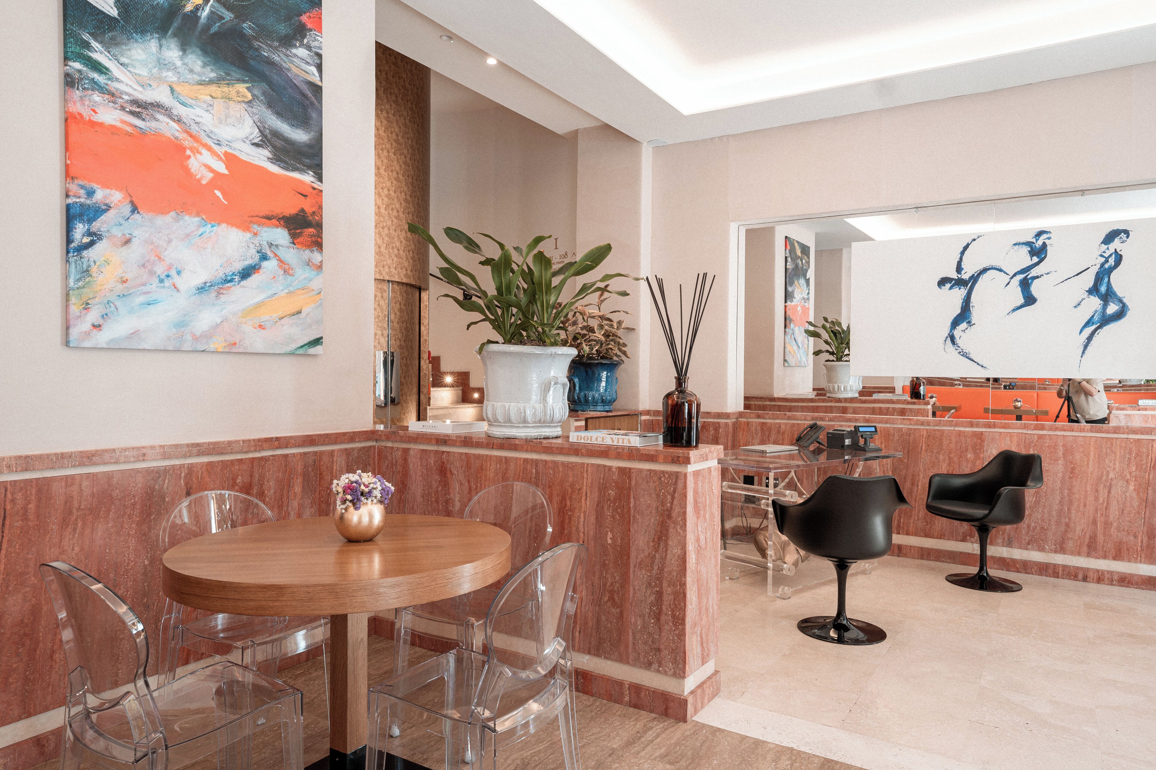 A modern hotel lobby with a marble reception desk, a round wooden table with chairs, and abstract art on the walls.