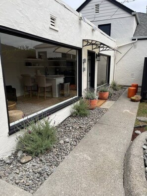 A modern house with a large glass window, a small outdoor seating area, and a pathway lined with potted plants. - Henderson Frog Pond Compound (Eureka)