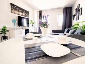 Una sala moderna con comedor, que incluye un televisor de pantalla plana, un sofá y una mesa de centro con un jarrón de flores.