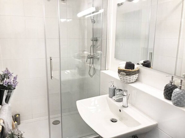 Un baño moderno con ducha envuelta en vidrio, un lavabo blanco con dispensador de jabón y un espejo sobre el lavabo.