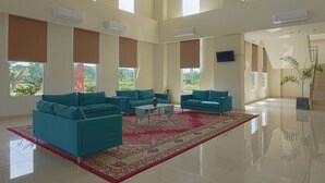 A spacious living area with teal sofas, a coffee table, and a red patterned rug. - OYO 3269 Hotel Grand Sayang Park Makassar (Makassar)