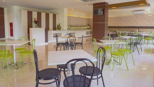 A spacious dining area with multiple tables and chairs, a reception desk, and a kitchen area in the background. - OYO 3269 Hotel Grand Sayang Park Makassar (Makassar)