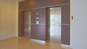 A hallway with two elevators, a control panel, and a red emergency button. - OYO 3269 Hotel Grand Sayang Park Makassar (Makassar)