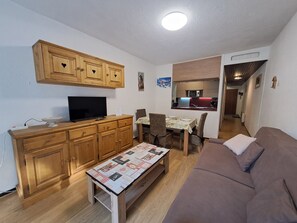 Un espacio habitable compacto con kitchenette, zona de comedor, sofá y televisor sobre un mueble de madera.