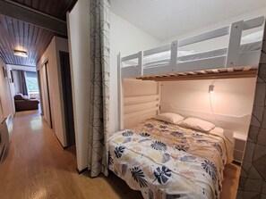 A bedroom with a bunk bed, a patterned bedspread, and a wooden floor. - Renovated studio, 4 pers, near slopes (Les Deux Alpes)