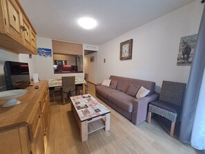 A living room with a sofa, a coffee table, a television, and a kitchen area in the background. - Renovated studio, 4 pers, near slopes (Les Deux Alpes)