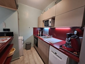Una cocina compacta con microondas, cafetera y lavamanos.