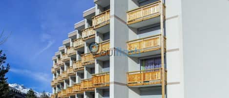 A multi-story hotel with balconies, a parking lot, and a mountainous backdrop.