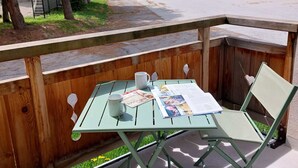 Une terrasse en bois avec une table et une chaise en métal vert, une tasse blanche et un magazine.