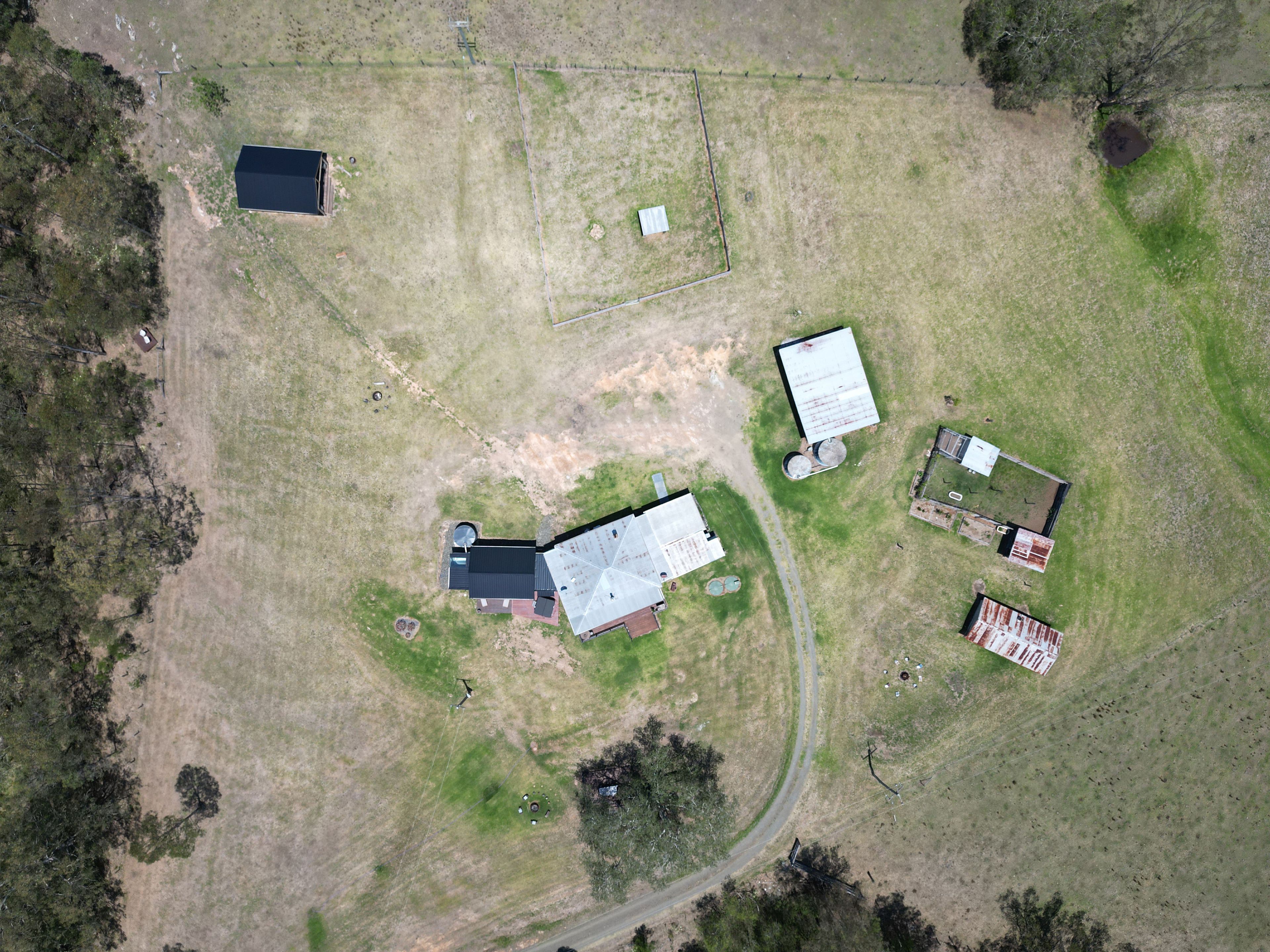 An aerial view of a property with multiple buildings, a fenced area, and a road.
