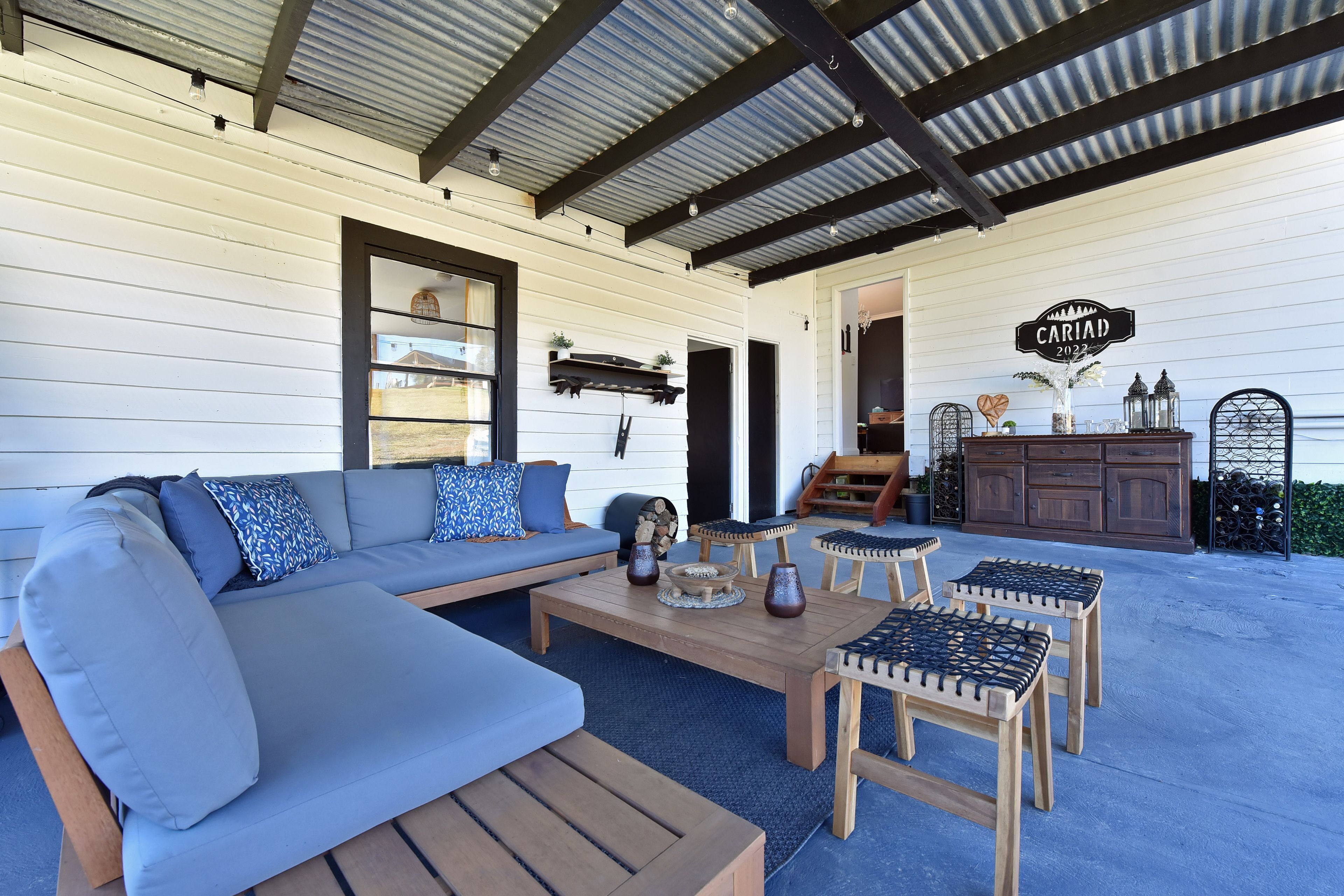 A covered outdoor seating area with a sofa, coffee table, and stools.