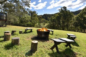 An outdoor setting with a fire pit, picnic tables, and wooden stumps.