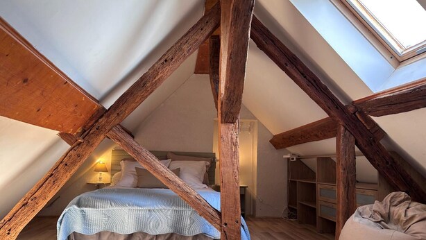 Een slaapkamer in loftstijl met zichtbare houten balken, een bed, een slaapzak en een dakraam.
