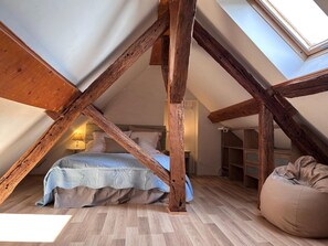 Camera soppalco con travi a vista in legno, un letto, un pouf e un lucernario.
