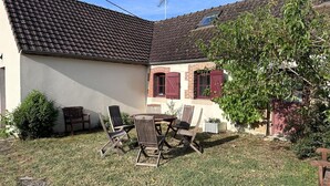 Een huis met een pannendak, een bakstenen schoorsteen en een kleine tuin met een tafel en stoelen.