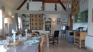 Een eetgedeelte met een tafel voor vier personen, een keuken op de achtergrond en een trap naar een hoger gelegen verdieping.