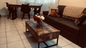 Un saló amb una taula de centre de fusta, un sofà, una taula de menjador amb caires i un ram de flors en un vas.