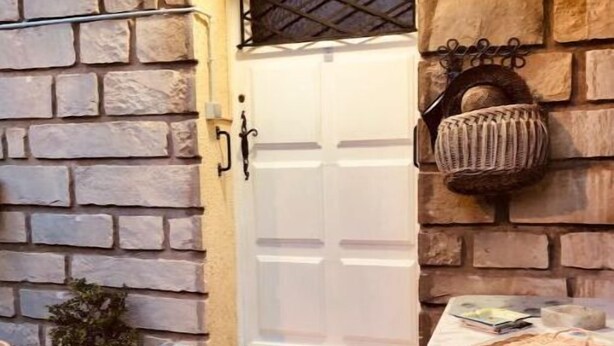 Entrada de pedra amb una porta blanca, un graó petit que hi mena i una taula amb objectes a sobre.