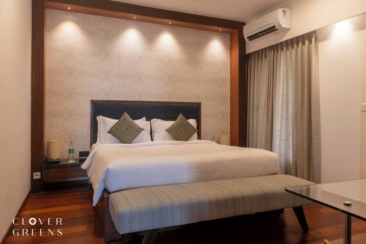 Una habitación de hotel con una cama grande, una mesita de noche con una lámpara y una mesa de vidrio.