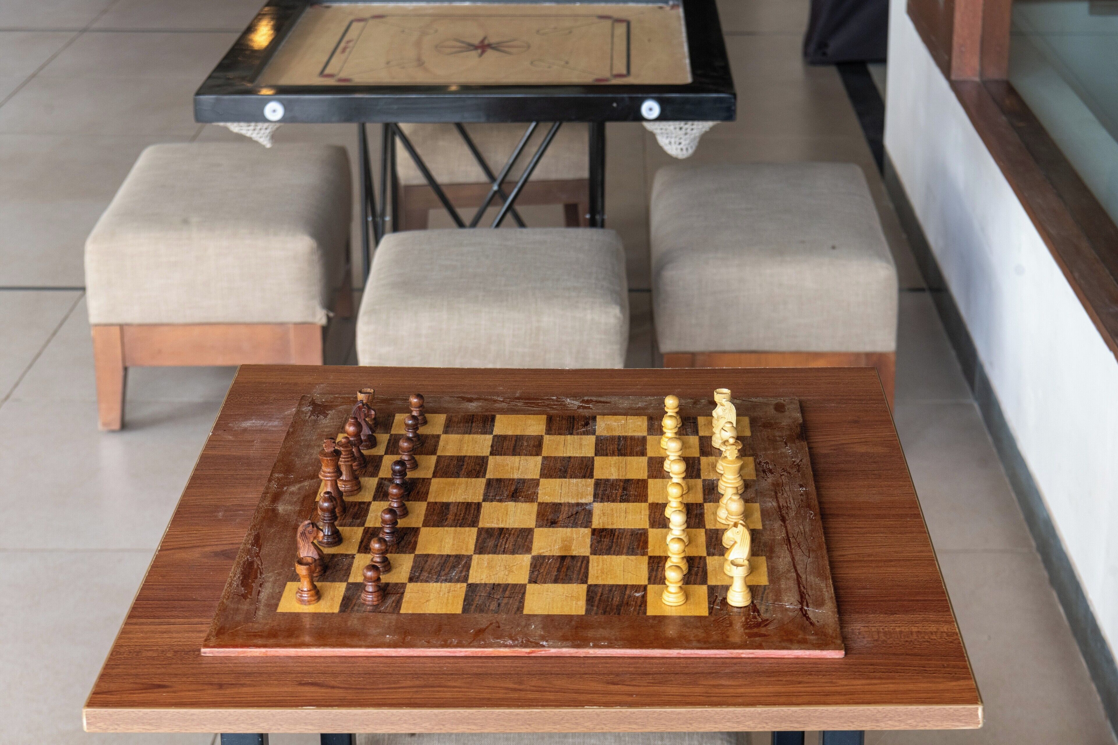 A wooden chessboard on a table with a checkered tablecloth underneath.