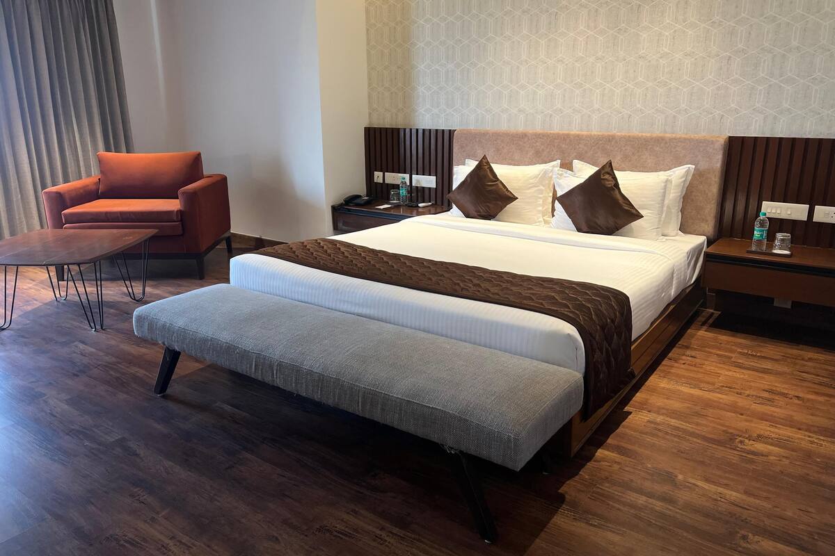 Una habitación de hotel con una cama grande, un sofá, una silla y piso de madera.