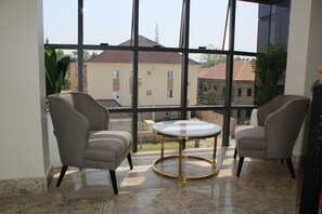 A room with two armchairs and a round table, large windows with a view of buildings, and a tiled floor. - Fahrenheit Hotel (Abuja)