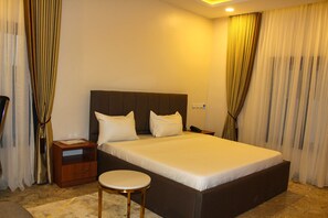 A neatly arranged hotel room with a large bed, bedside tables, and a small round table. - Fahrenheit Hotel (Abuja)