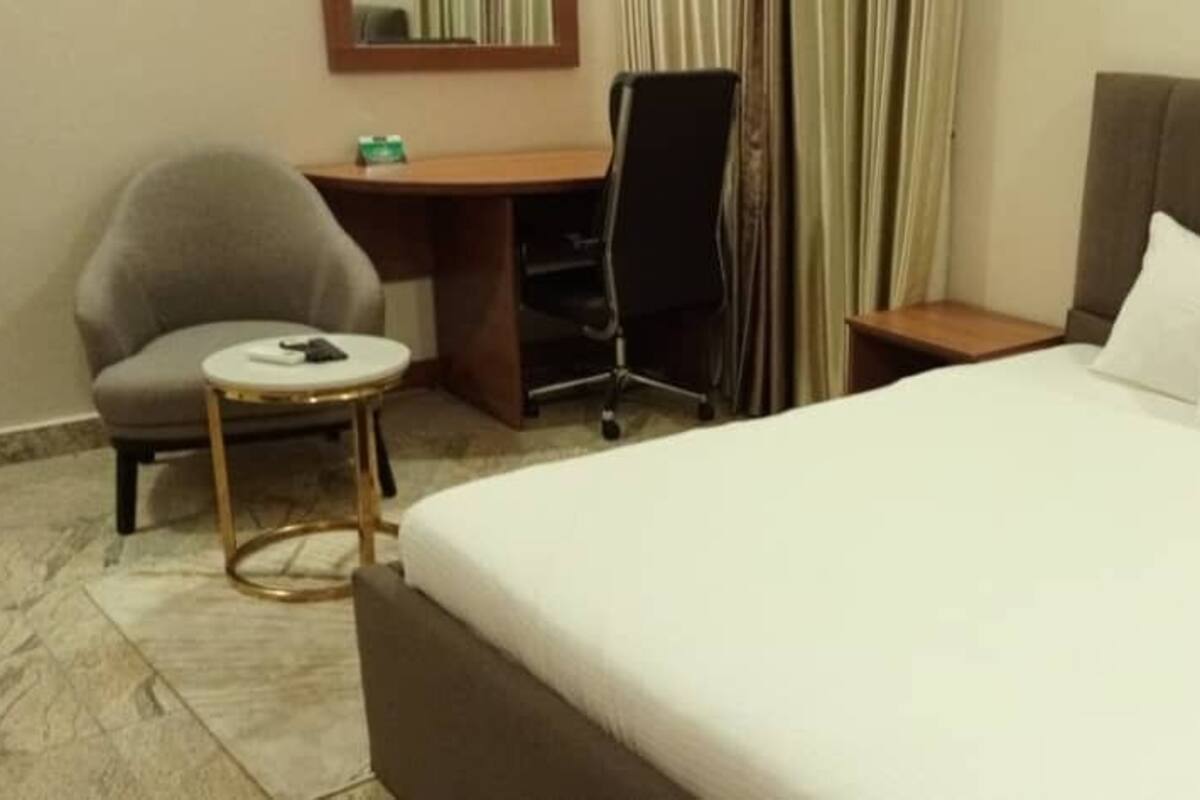 A hotel room with a large bed, a desk, a chair, and a small round table.