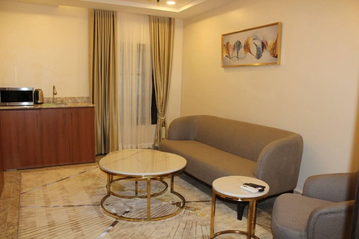 A compact living space with a sofa, two round tables, a kitchenette, and a painting on the wall.