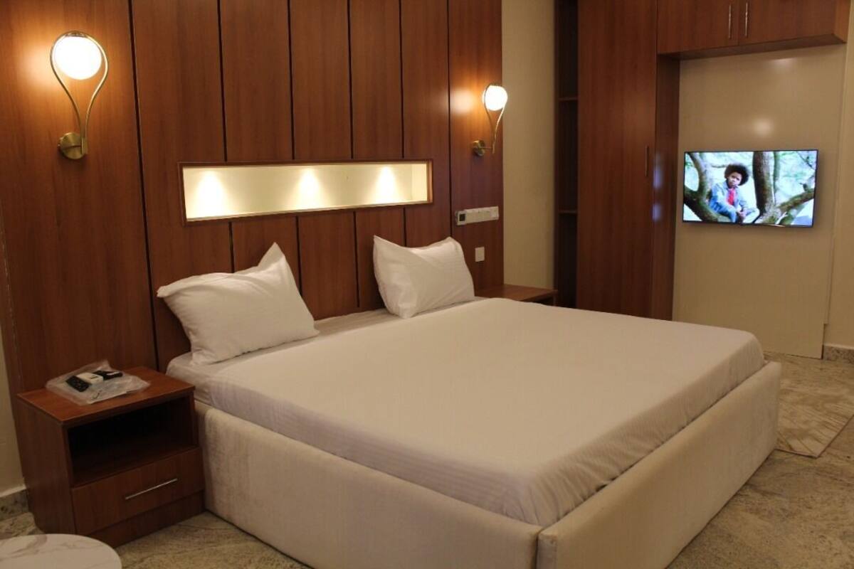 A hotel room with a large bed, wooden panel walls, two bedside lamps, a flat-screen TV, and a nightstand with a drawer.