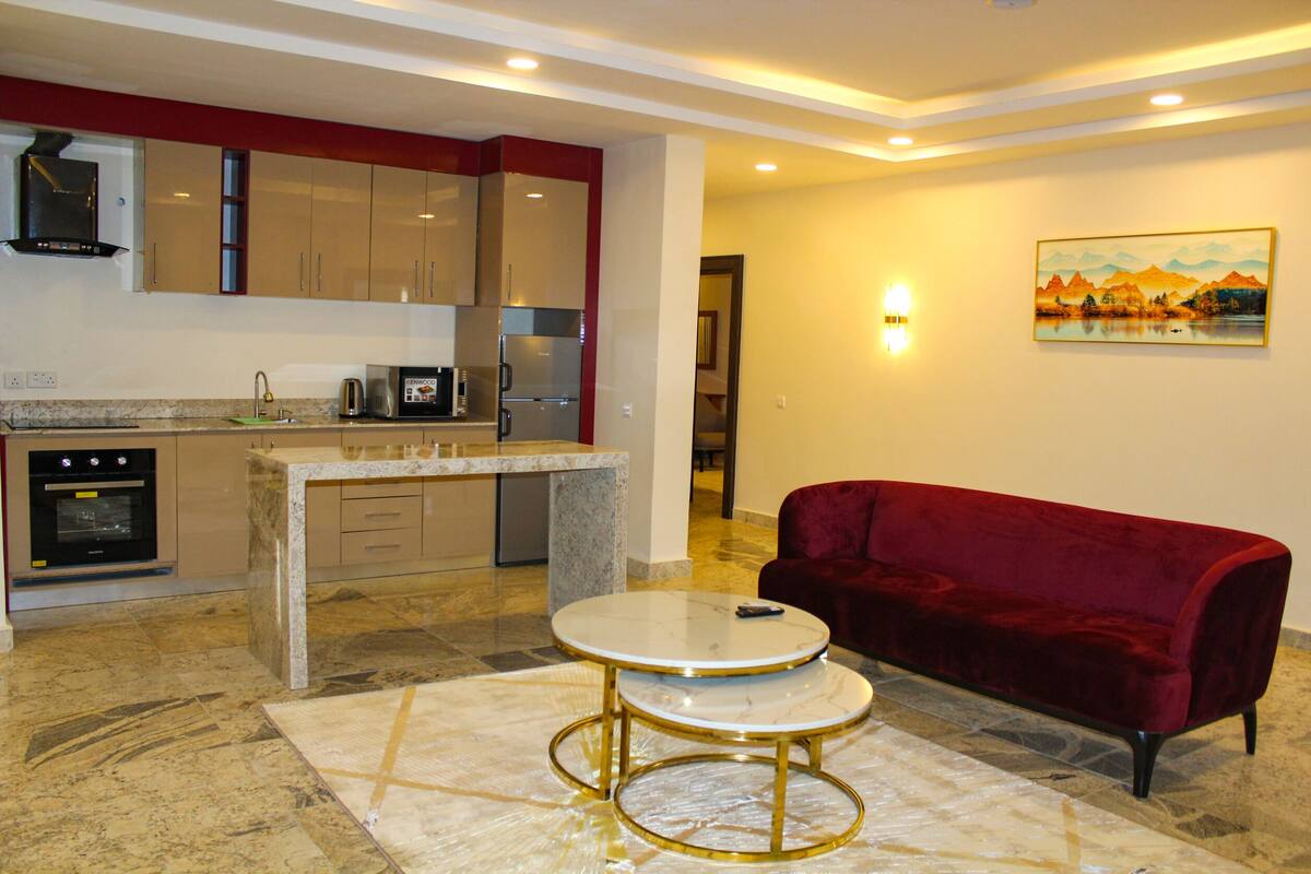 A modern kitchen with granite countertops, stainless steel appliances, and a red velvet sofa in a living area with a marble floor.