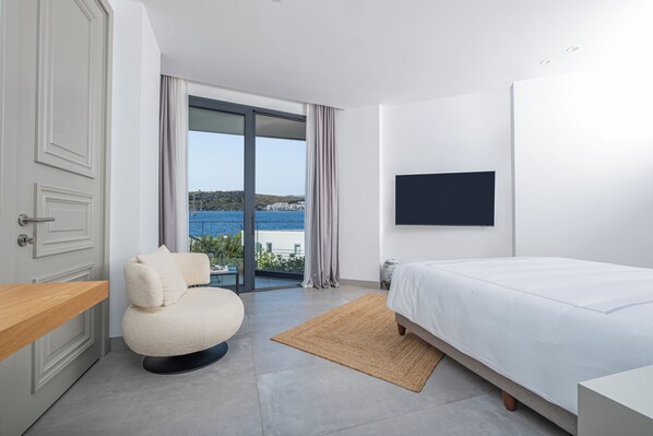 Ein modernes Schlafzimmer mit Bett, Stuhl, Fernseher und Meerblick.