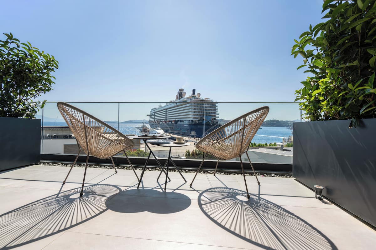 A balcony with two wicker chairs facing a large cruise ship.