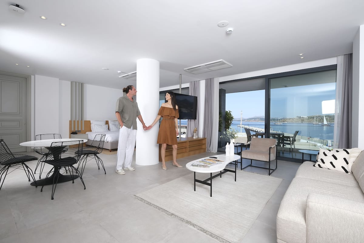 A modern living room with a large window, a dining area with a round table, and a sofa.