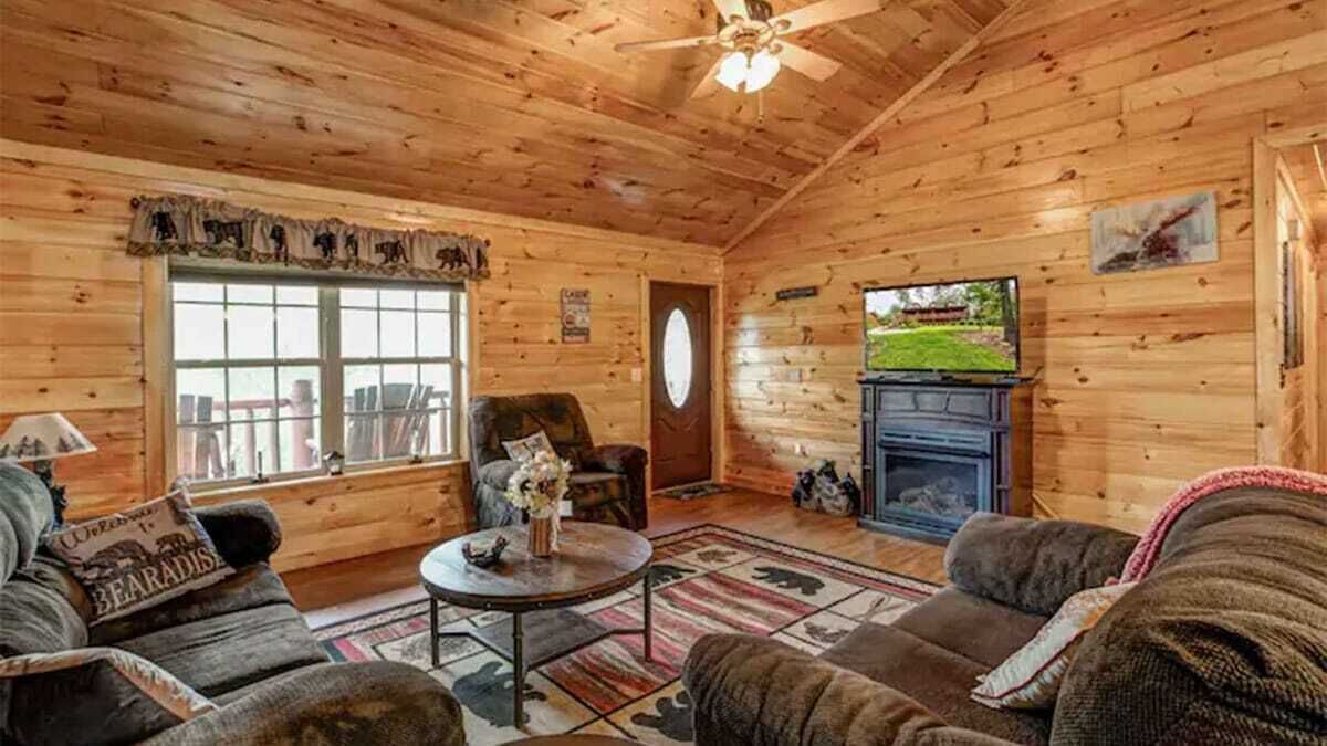 A cozy cabin interior with wooden walls, a fireplace, a television, and a comfortable seating area.