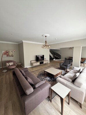 Una sala de estar moderna con un juego de sofás, una mesa de centro, un mueble para televisor y una escalera que sube a otro nivel.