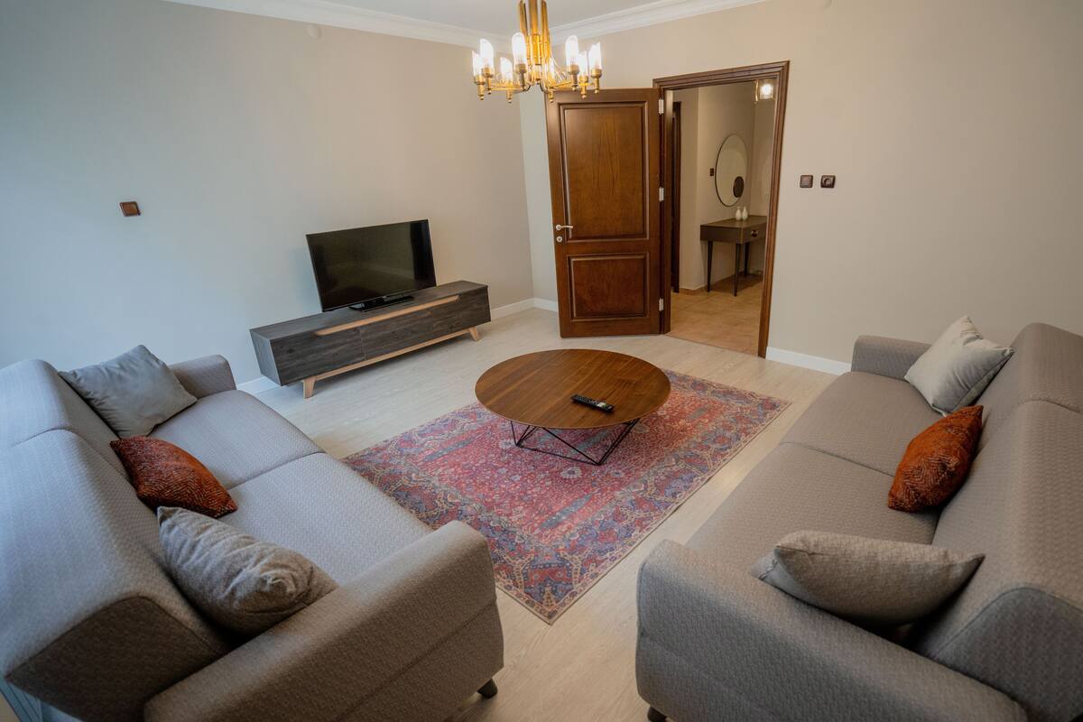 A living room with two sofas, a coffee table, a TV, and a wooden door leading to a bathroom.