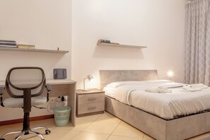 Ein Schlafzimmer mit Bett, Schreibtisch mit Stuhl, Nachttisch und einer Wandregal mit Büchern.