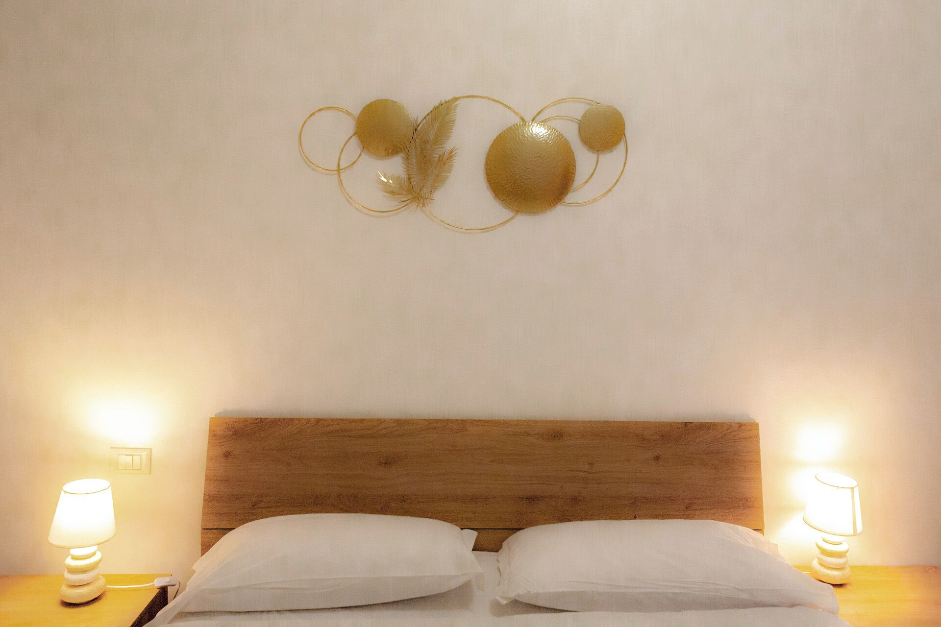 A bedroom with a wooden headboard, two bedside lamps, and a wall art piece above the bed.