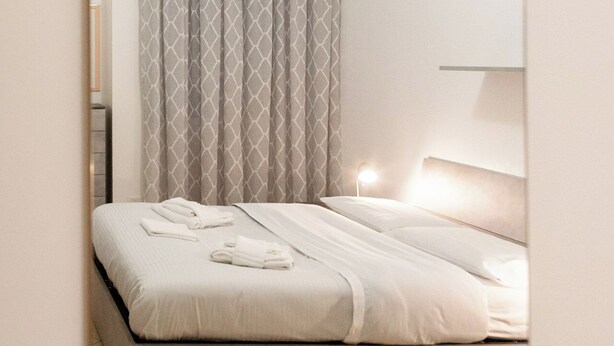 A neatly made bed with a white duvet and a grey patterned curtain. - BnButler - Pellegrino Rossi 42 (Milan)